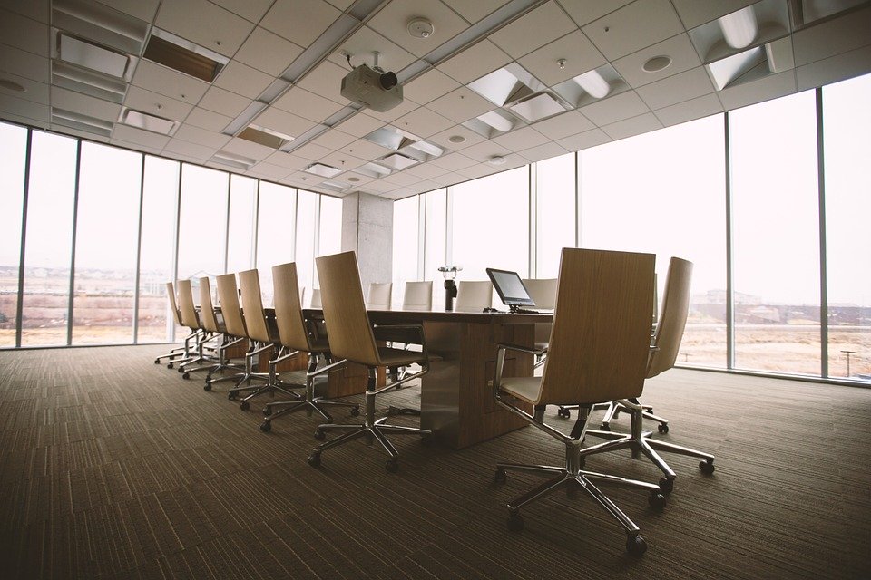 La imagen muestra una sala de reuniones vacía con una mesa alargada y muchas sillas