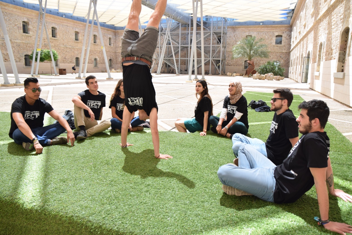 Se muestra un grupo de estudiantes en el patio de la Facultad de Ciencias de la Empresa. Uno de ellos está haciendo el pino y los demás le miran